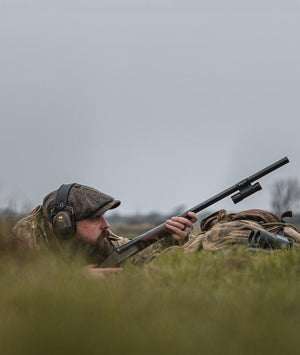 Hunter in camouflage gear with a rifle in a cold field for bird season